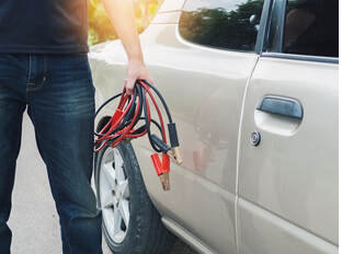Picture of a man walking next to his car with a pair of jumper cables in his hand.