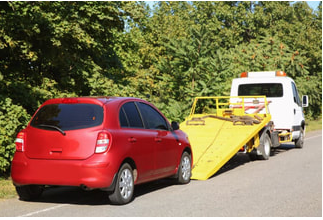 Picture of a red hatchback car getting ready to be moved on a light duty tow truck.