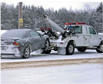 Picture a white tow truck hauling a gray car through the snowy road on its way to its next destination.