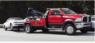 Picture of a white car being towed by a red tow truck. The vehicle its being towed to its final destination.